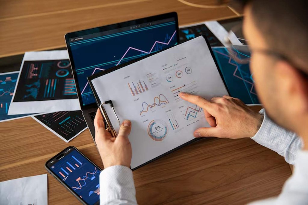 Financial analyst reviewing performance charts on paper and digital screens, illustrating the complexity and data-driven nature of cross-border investment strategies between markets.