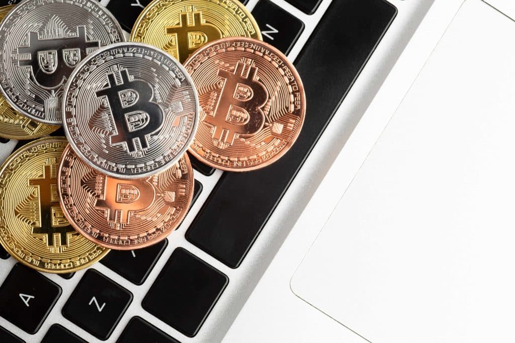 Physical representations of cryptocurrencies, including gold, silver, and bronze Bitcoin tokens, displayed on a laptop keyboard, symbolizing digital asset trading and investment.