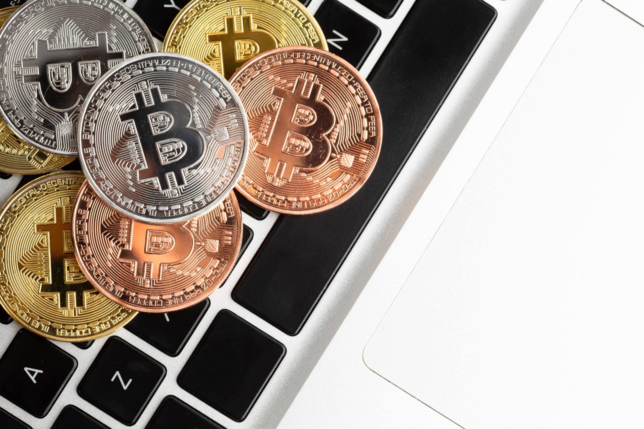 Physical representations of cryptocurrencies, including gold, silver, and bronze Bitcoin tokens, displayed on a laptop keyboard, symbolizing digital asset trading and investment.