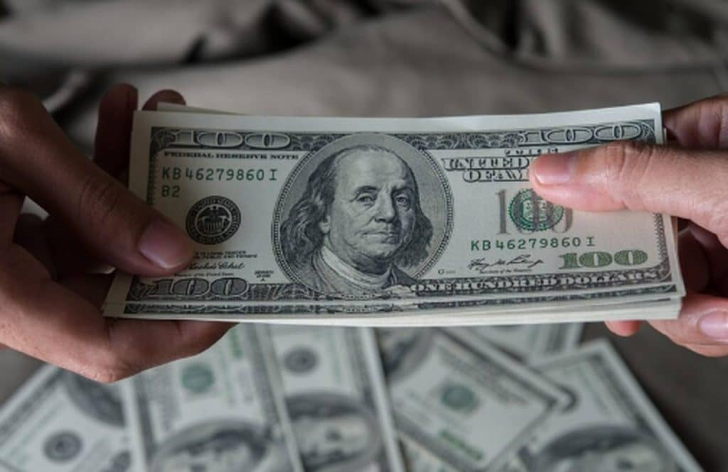 A close-up of hands exchanging a stack of U.S. hundred-dollar bills, symbolizing physical money and traditional cash transactions.