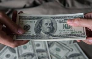 A close-up of hands exchanging a stack of U.S. hundred-dollar bills, symbolizing physical money and traditional cash transactions.