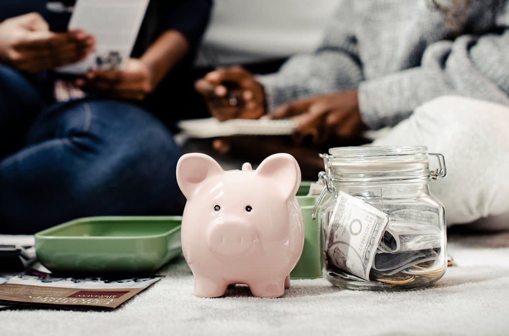 A pink piggy bank beside a glass jar filled with dollar bills and coins, symbolizing savings and financial planning within the domestic economy.