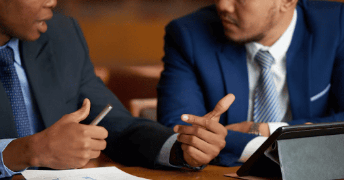 Two businessmen in suits discussing financial information and documents during a meeting.