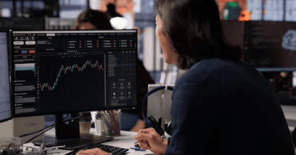 Person analyzing stock market charts on a computer screen in an office, reviewing finances and investment data.