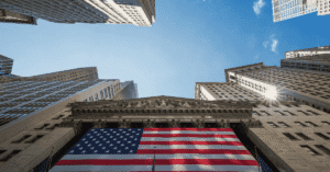 Upward view of Wall Street buildings surrounding a large American flag displayed on a historic financial building, symbolizing information about U.S. markets, economy, and financial institutions.